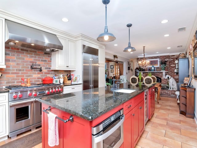 kitchen featuring wall chimney range hood, premium appliances, crown molding, an island with sink, and white cabinets