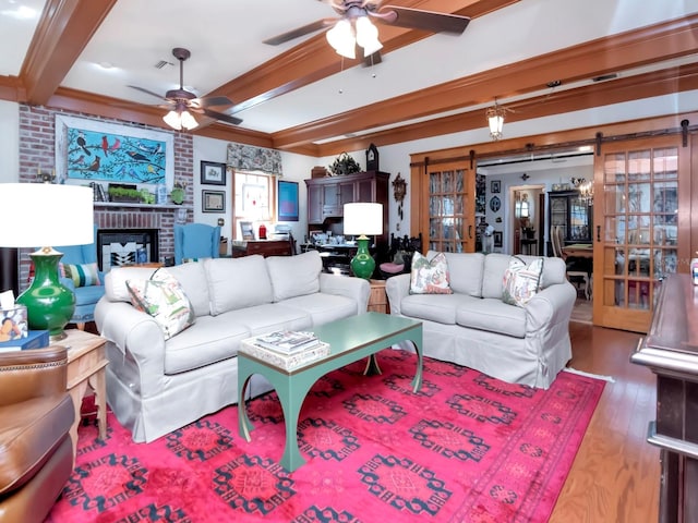 living room with ornamental molding, ceiling fan, beam ceiling, a barn door, and hardwood / wood-style floors