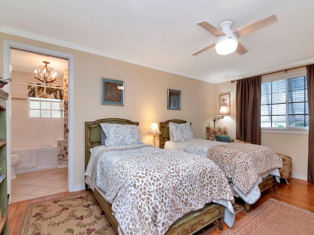 bedroom featuring ceiling fan with notable chandelier, ensuite bathroom, light wood-type flooring, and crown molding