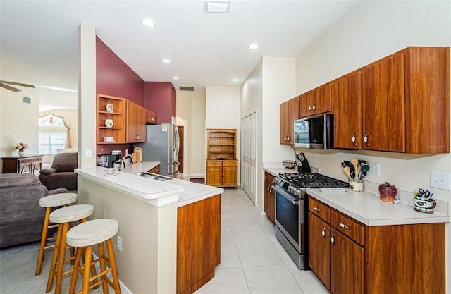 kitchen with kitchen peninsula, appliances with stainless steel finishes, a kitchen breakfast bar, sink, and light tile patterned floors