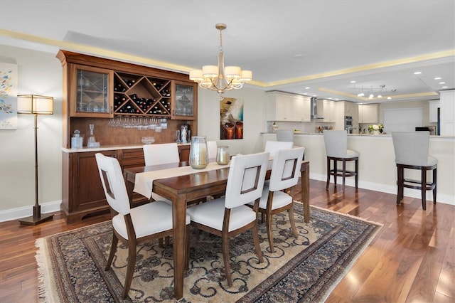 dining area with dark wood-type flooring, a raised ceiling, bar area, a chandelier, and ornamental molding