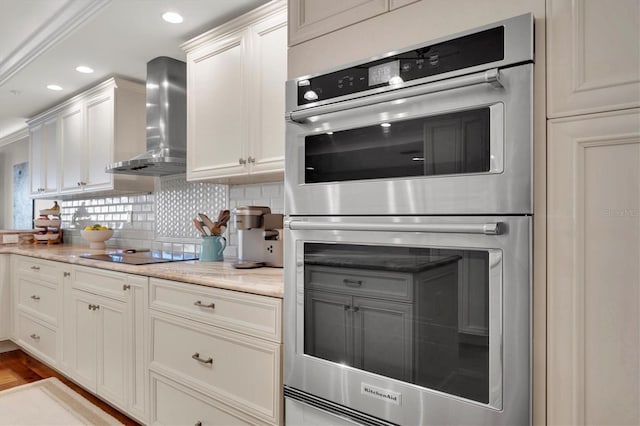 kitchen with black electric stovetop, wall chimney exhaust hood, double oven, light stone counters, and white cabinetry