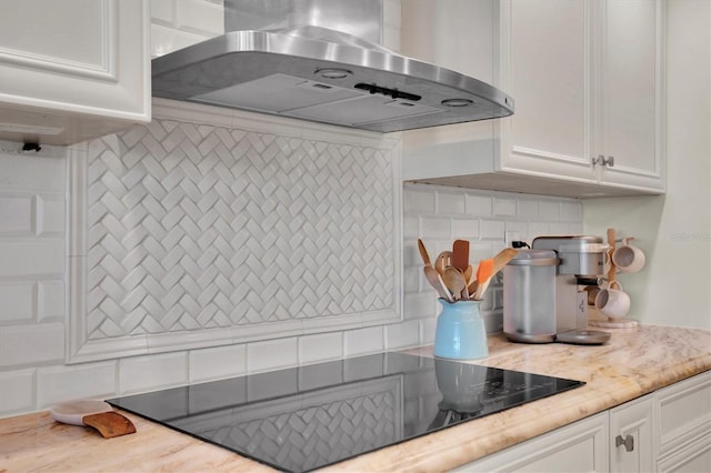 kitchen with decorative backsplash, white cabinets, and wall chimney range hood