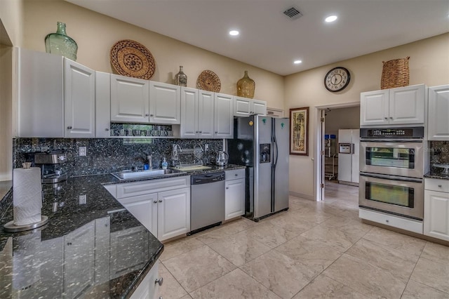 kitchen featuring white cabinetry, sink, stainless steel appliances, backsplash, and dark stone counters