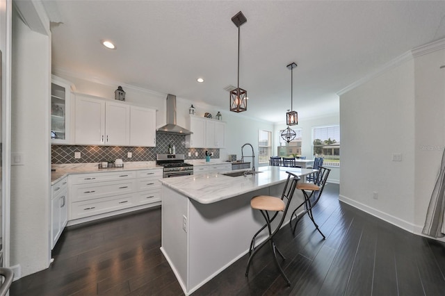 kitchen with white cabinets, a center island with sink, wall chimney range hood, sink, and gas range