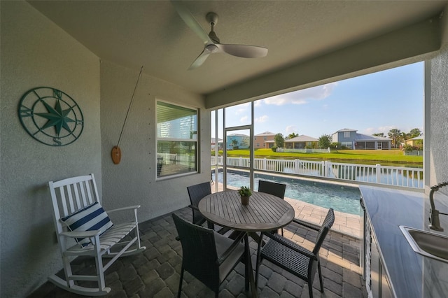 sunroom with ceiling fan, a water view, and a pool