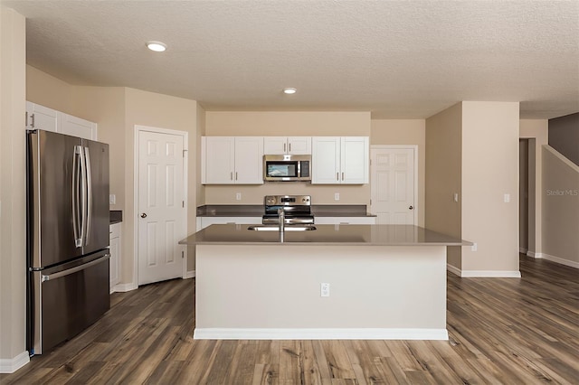 kitchen with stainless steel appliances, white cabinetry, a kitchen island with sink, and dark wood-type flooring