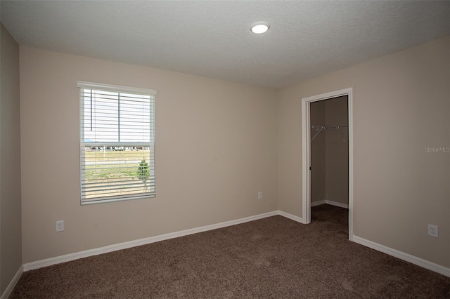 unfurnished bedroom with a spacious closet, a closet, a textured ceiling, and dark colored carpet