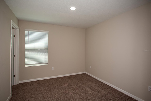 spare room featuring a textured ceiling and dark colored carpet