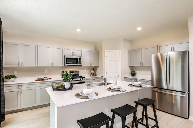 kitchen featuring sink, light hardwood / wood-style flooring, an island with sink, appliances with stainless steel finishes, and a kitchen bar