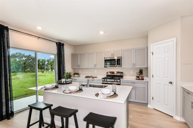 kitchen with gray cabinetry, a kitchen island with sink, sink, and appliances with stainless steel finishes