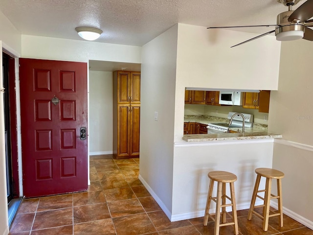 kitchen featuring ceiling fan, kitchen peninsula, a textured ceiling, white appliances, and a breakfast bar area