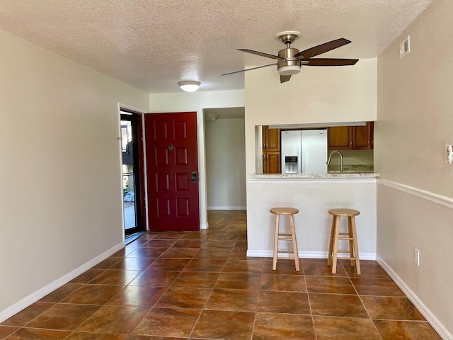 kitchen featuring ceiling fan, stainless steel fridge, a textured ceiling, kitchen peninsula, and a breakfast bar area