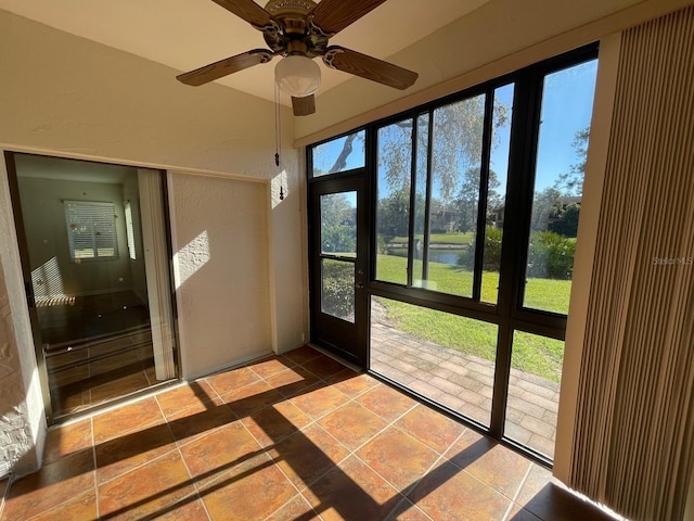 unfurnished sunroom featuring ceiling fan and a water view