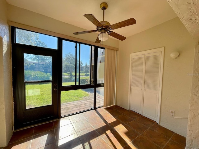 doorway with dark tile patterned flooring and ceiling fan