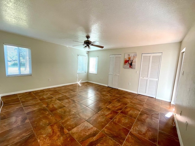 unfurnished bedroom with a textured ceiling, two closets, and ceiling fan