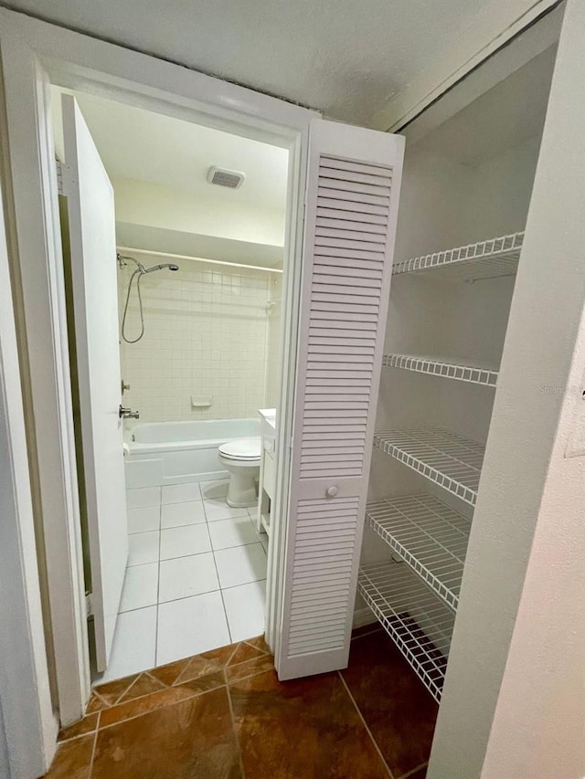 bathroom with tile patterned floors, tiled shower / bath combo, and toilet