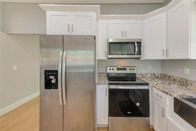 kitchen with white cabinets, stainless steel appliances, light stone counters, and light hardwood / wood-style floors