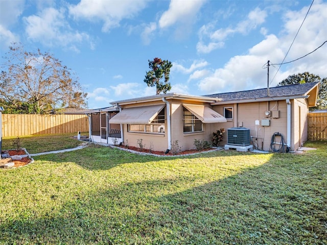 rear view of house featuring central AC unit, a yard, and a sunroom