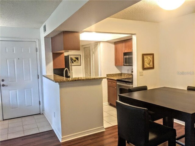 10200 Gandy Blvd N Unit 921, Saint Petersburg, FL 33702 - kitchen featuring stainless steel appliances, a peninsula, tile patterned floors, a textured ceiling, and brown cabinetry