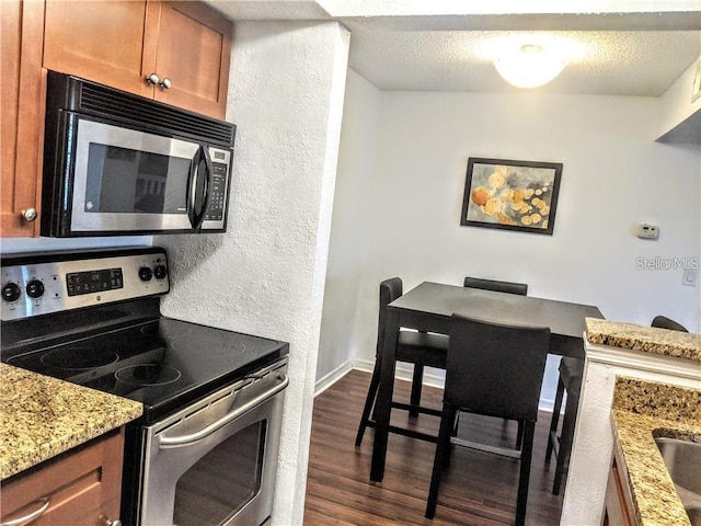10200 Gandy Blvd N Unit 921, Saint Petersburg, FL 33702 - kitchen featuring appliances with stainless steel finishes, brown cabinets, dark wood-style floors, a textured wall, and light stone counters