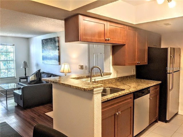 kitchen with kitchen peninsula, appliances with stainless steel finishes, light stone counters, sink, and light hardwood / wood-style flooring