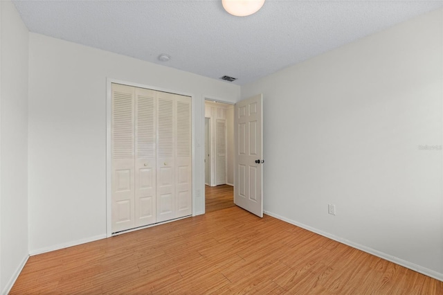 unfurnished bedroom with a textured ceiling, light wood-type flooring, and a closet