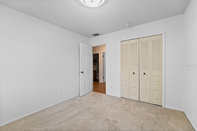 unfurnished bedroom featuring light carpet, a textured ceiling, and a closet