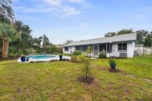 back of property with central AC unit, a sunroom, a fenced in pool, and a yard