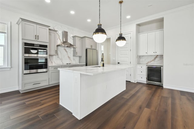 kitchen featuring light stone countertops, gray cabinetry, a kitchen island with sink, dark wood-type flooring, and wall chimney range hood