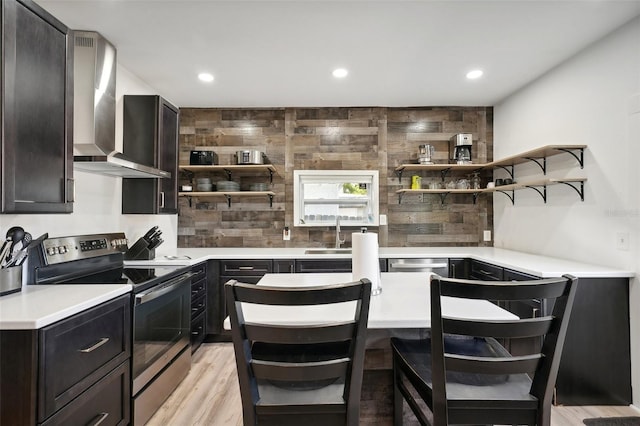 kitchen featuring decorative backsplash, a kitchen breakfast bar, wall chimney exhaust hood, stainless steel appliances, and light hardwood / wood-style flooring