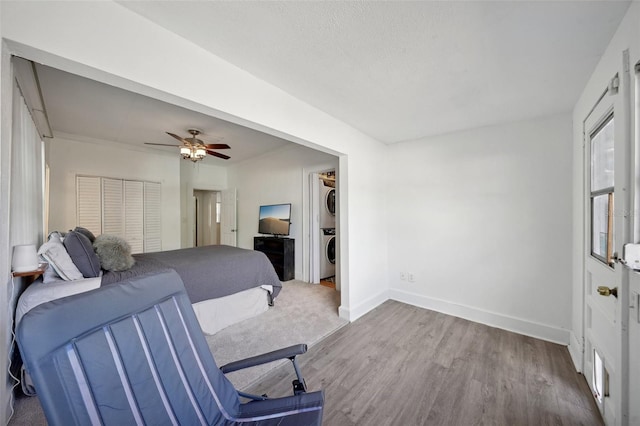 bedroom with a closet, stacked washer / dryer, ceiling fan, and hardwood / wood-style floors