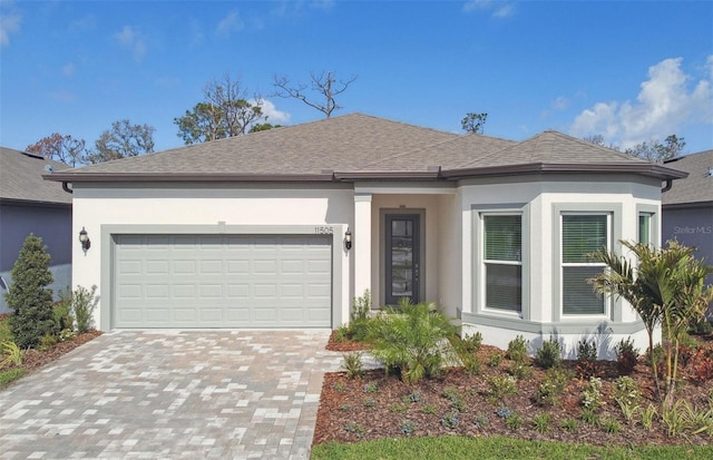 view of front facade with a shingled roof, decorative driveway, a garage, and stucco siding