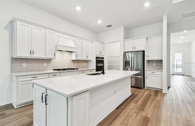 kitchen with visible vents, stainless steel fridge with ice dispenser, custom range hood, gas cooktop, and a sink