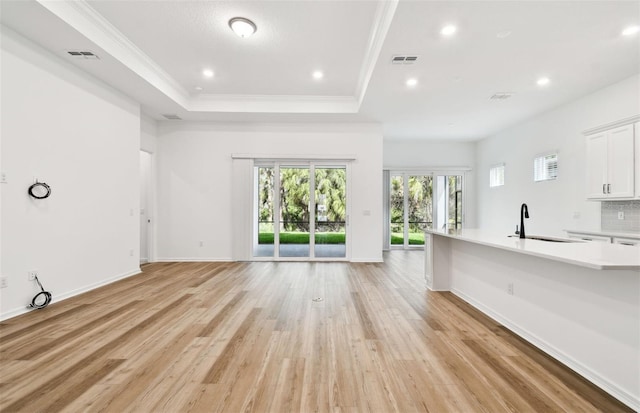 unfurnished living room with recessed lighting, a sink, ornamental molding, light wood-type flooring, and a raised ceiling