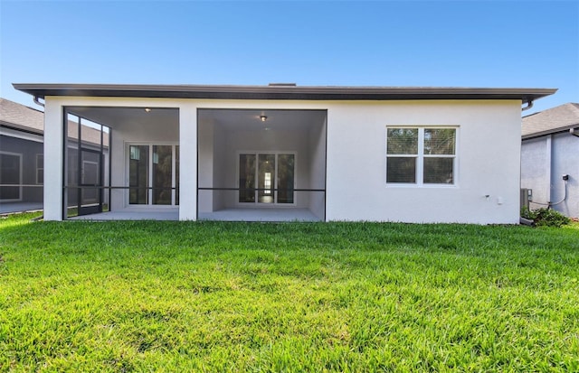 rear view of house with a lawn, a sunroom, and stucco siding