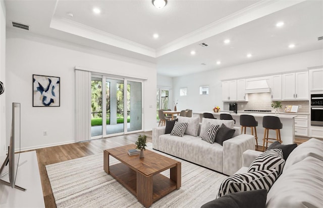 living room featuring visible vents, a raised ceiling, ornamental molding, light wood-style floors, and recessed lighting