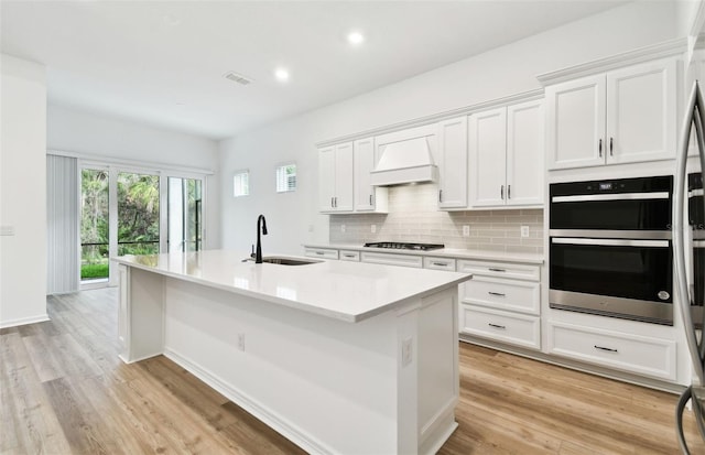 kitchen featuring stainless steel gas cooktop, decorative backsplash, double oven, a sink, and premium range hood