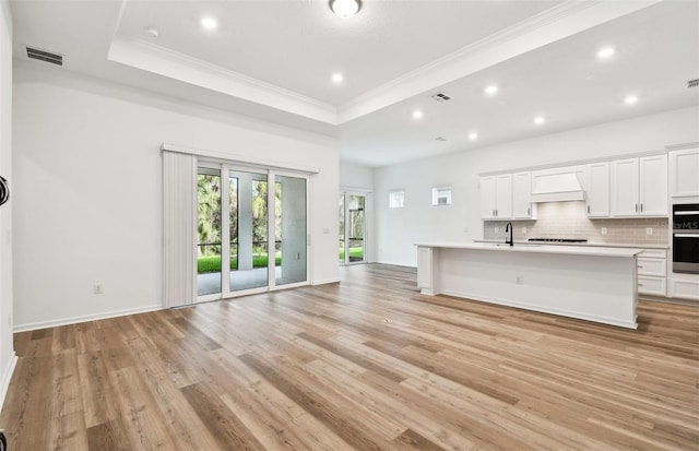 kitchen with visible vents, a raised ceiling, decorative backsplash, open floor plan, and premium range hood