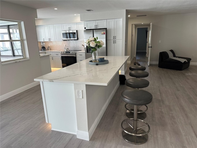 kitchen featuring hardwood / wood-style flooring, white cabinetry, a breakfast bar area, and appliances with stainless steel finishes