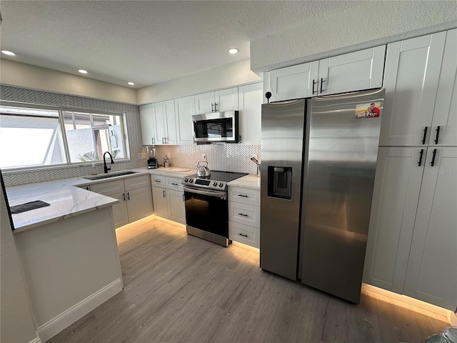 3963 Glen Oaks Manor Dr, Sarasota, FL 34232 - kitchen featuring appliances with stainless steel finishes, a sink, white cabinets, light stone counters, and light wood finished floors