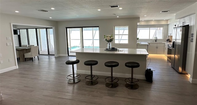 kitchen with a kitchen island, dark hardwood / wood-style floors, stainless steel fridge, a kitchen bar, and white cabinets