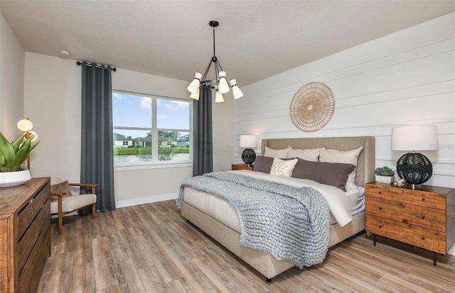 bedroom with a chandelier, a water view, a textured ceiling, and light hardwood / wood-style flooring