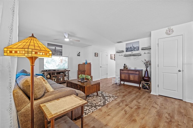 living room with ceiling fan, a textured ceiling, and light wood-type flooring