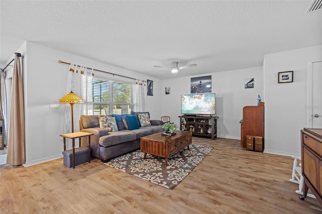 living room featuring ceiling fan, a textured ceiling, and light wood-type flooring