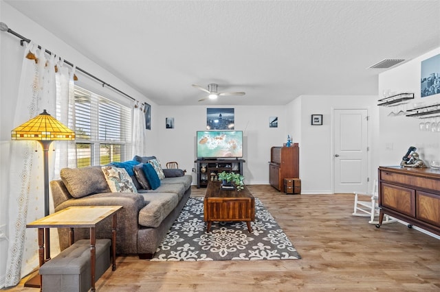 living room with ceiling fan, light hardwood / wood-style flooring, and a textured ceiling