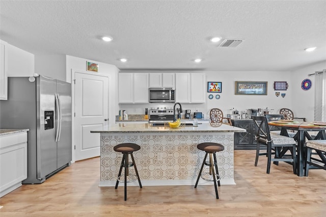 kitchen with appliances with stainless steel finishes, a kitchen breakfast bar, a kitchen island with sink, light hardwood / wood-style flooring, and white cabinetry