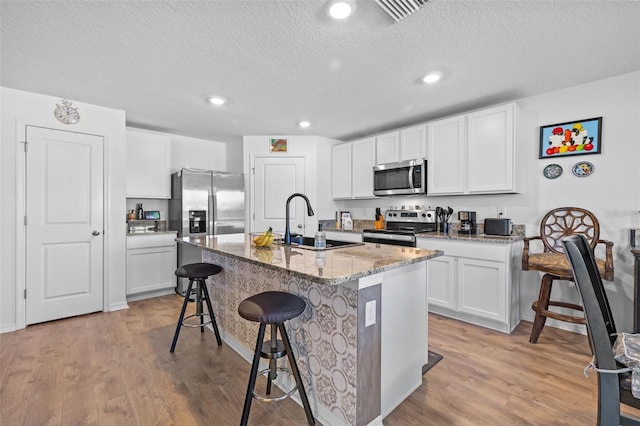 kitchen featuring white cabinets, stainless steel appliances, a kitchen island with sink, and a breakfast bar area