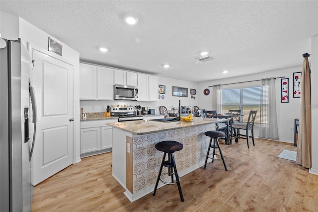 kitchen featuring appliances with stainless steel finishes, light wood-type flooring, a kitchen breakfast bar, a kitchen island with sink, and white cabinets