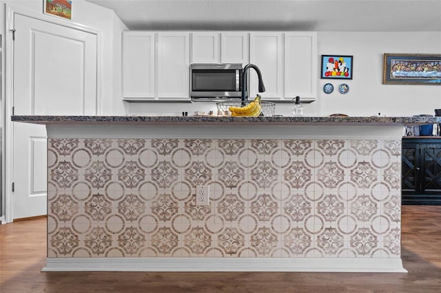 kitchen with white cabinets, wood-type flooring, and an island with sink